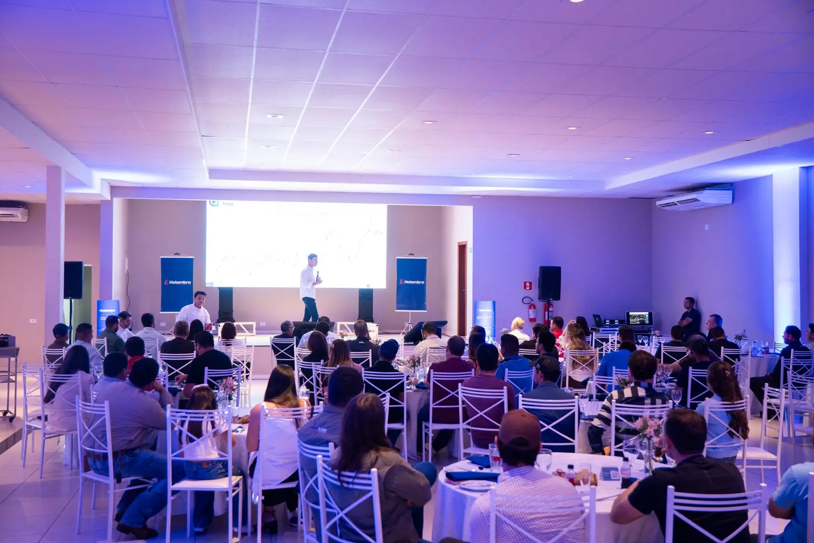 Salão de eventos com plateia acompanhando palestra